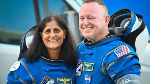 Two Nasa astronauts - Suni Williams and Butch Wilmore - in blue spacesuits, smiling at camera