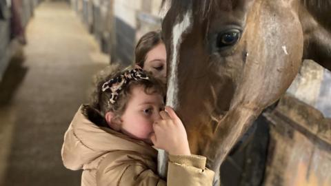 Betsy kisses Kitty's Light in the stables with her sister Tilly alongside her