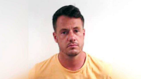 A mugshot of Cameron Ross, looking straight at the camera wearing a yellow T-shirt against a white background.