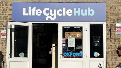 The front of the Life Cycle hub in Derby. It is a brick building with a white front door and a sign saying "Life Cycle Hub"