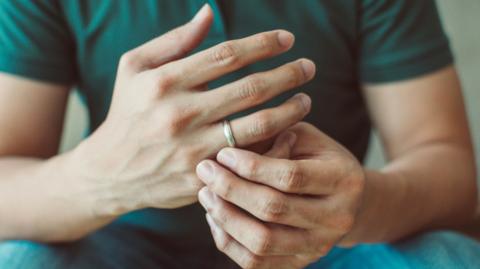 A man with a wedding ring clasps his hands