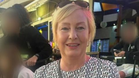 A woman with blond hair and sunglasses on her head smiles for the camera
