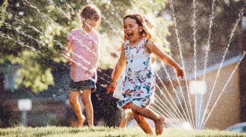 Girl in a summer dress running through a sprinkler