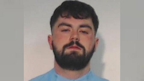 Police mugshot of Dylan Nicol who has dark hair and a beard