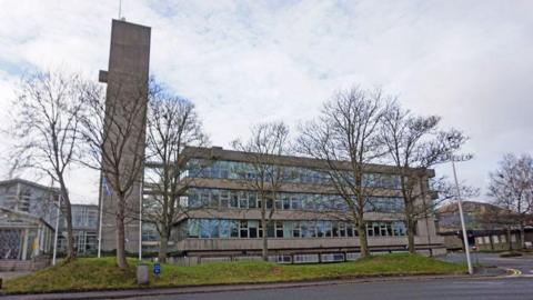 A grey industrial looking building with a lot of windows, a tower and a Scottish flag flying outside - Scottish Borders Council's headquarters building