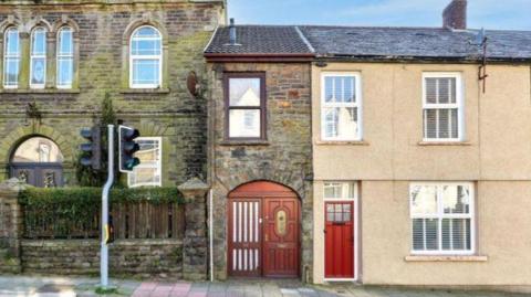 A general view of property on Llewellyn Street. It is a brick house with a wooden door and window frame. The house sits on the main street in front of a set of traffic lights.