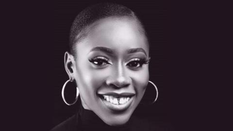 Chinenye Okonkwo is smiling at the camera. Her black hair is scraped back and she is pictured against a black backdrop. She is wearing large, hooped earrings