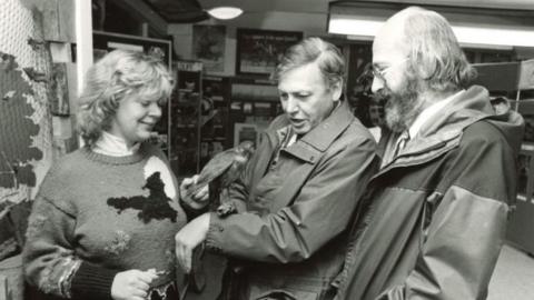 Sir David Attenborough pictured at the Surrey Wildlife Trust centre at Nower Wood near Leatherhead. The picture, taken in 1985, is in black and white. Sir David is stood beside two people at the centre, and has a bird on his left arm.