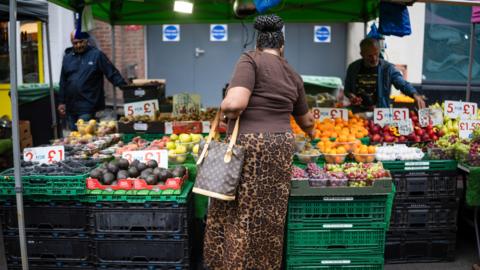 A woman in a leopard print skirt and brown top pics out fruit at a market