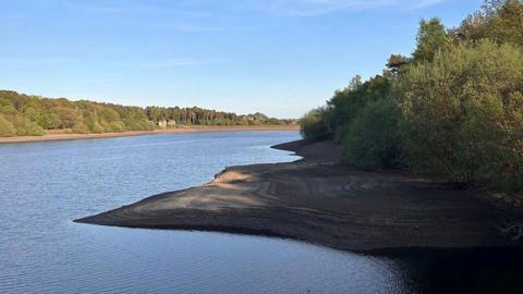 A reservoir in Yorkshire, with exposed banks suggesting the water level is lower than usual. The weather is bright and clear. 
