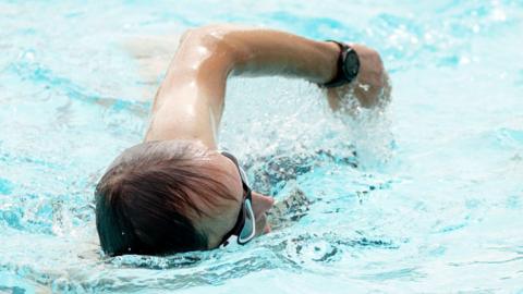 A person swims through pool water. The swimmer is wearing goggles and a water. 