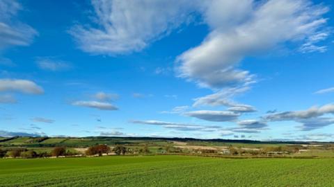 Blue sky with white clouds over green fields and hills 