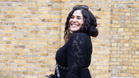 Gemma Devonish, a woman with long, dark hair, smiling and wearing a black dress 