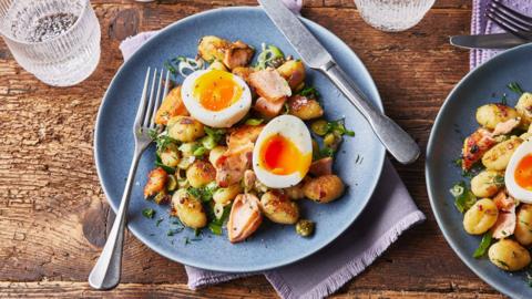 Salmon gnocchi with two halves of an egg on top sits on a blue plate with a knife and fork on the side