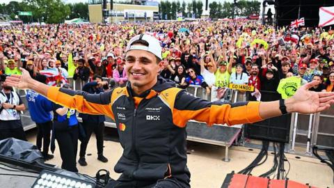 Lando Norris celebrates with fans after winning the British Grand Prix, holding his arms outstretched
