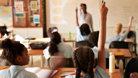 A generic view of students in a classroom, with three pupils raising their hands.