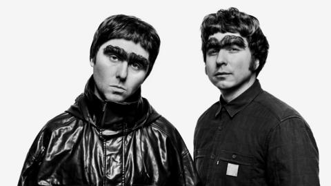 James Buckley (left) and Joe Thomas recreate the Oasis reunion picture. James, as Liam Gallagher, wears a shiny black coat zipped up to his chin. Joe, as Noel, wears a black buttoned up shirt. They both have short hair, fringes and giant novelty eyebrows.