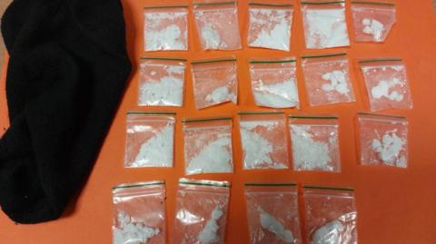 The 19 wraps of cocaine laid out on an orange table next to the black sock they have been found in.