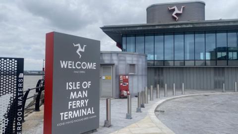 The new Liverpool ferry terminal, a grey building with bollards in front and a sign welcoming passengers to the left of the image 