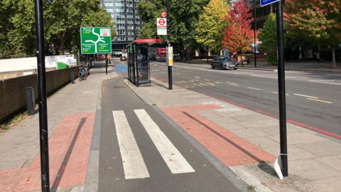 A bus stop (right) next to the road and a pedestrian crossing in the foreground