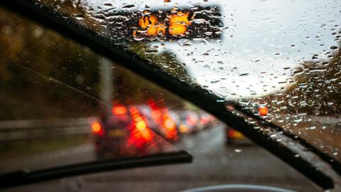 A stock image of a rainy windscreen of a car waiting in traffic on a motorway