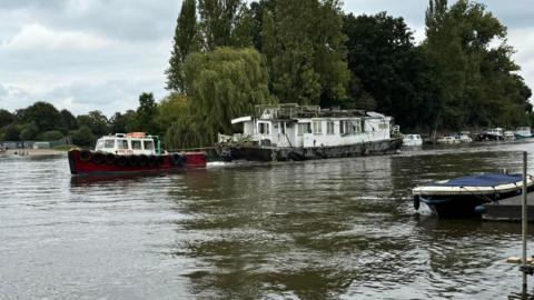 A white boat is being towed away by a red boat. 