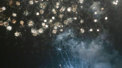 A series of pale-coloured fireworks light up the night sky.