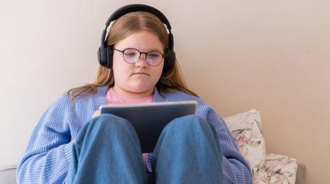 GCSE biology image: a teenager sits up in their bedroom with a tablet and headphones, studying.