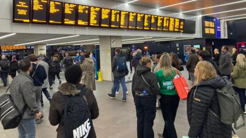 A group of passengers stare at information boards at Leeds Station