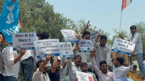 Protesters standing on barricades holding placards which read the medical entrance test is compromised as police personnel push them back