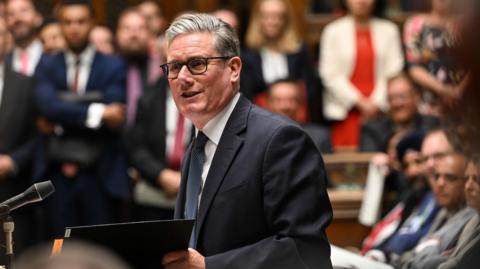 Starmer is pictured at last week's PMQs - he's wearing a navy suit, white shirt and blue tie; he's standing and talking