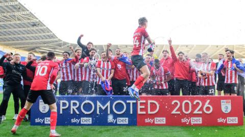 Lincoln City players and staff celebrate their promotion from League One with by spraying champagne 
