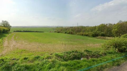 A green field site with a rural road alongside 