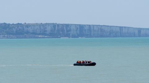 A small boat sails on a pale blue ocean.