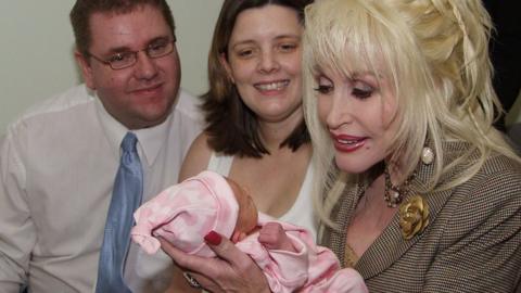 A glamorous Dolly Parton holds a newborn baby as mum and dad look on in Rotherham hospital