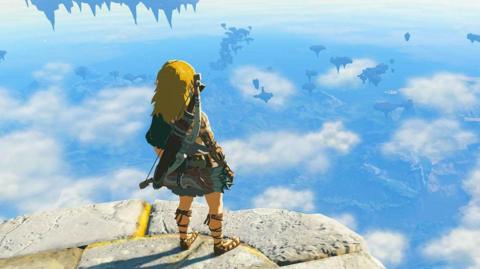 A screenshot from a video game showing a character, with long blond hair, a tunic and carrying a bow and arrows on his back, standing on the edge of a stone platform looking over a fantasy skyscape.