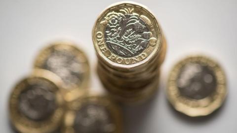 A stack of £1 coins seen from above with other £1 below roundabout.