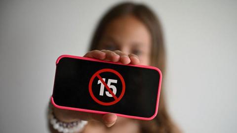 A teenager holds her smartphone displaying a logo "ban under 15" i
