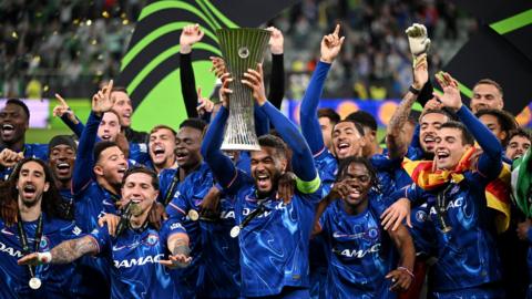 Chelsea captain Reece James lifting the Conference League trophy surrounded by his happy teammates.
