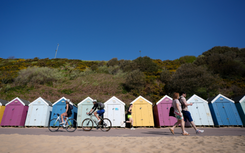 People make their way past beach huts on Bournemouth beach in Dorset.