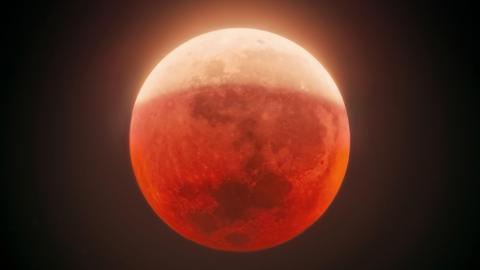 A red-coloured full Moon in partial lunar eclipse against a dark night sky
