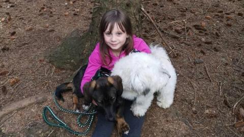 Freya Skene - a young girl with brown hair and a pink top, sitting outdoors with a dog on her lap