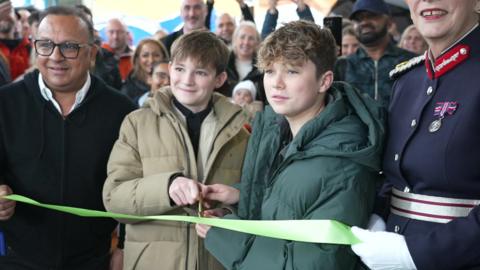 Hughie and Freddie cutting a green ribbon which is held in front of them