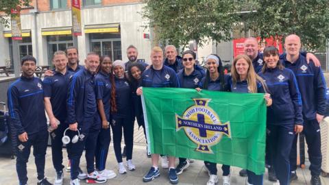 The NI team stands with the NI flag. 