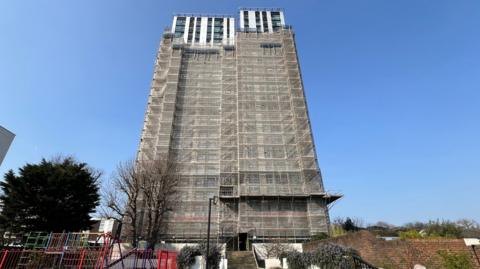 Dorney House tower block covered in tarpaulin except upper four floors set against blue sky