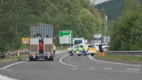 Police vehicles block a motorway as they deal with a collision. Other vehicles with drivers standing beside them are visible