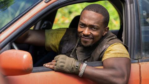 Anthony Mackie, in an orange car. he is wearing yellow tshirt with green waistcoat