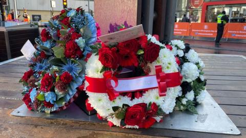 A wreath of white, red and blue flowers laid at the bottom of a memorial