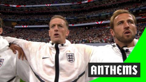Jordan Pickford with his arm around Harry Kane in the middle of the pitch as they sing England's national anthem.