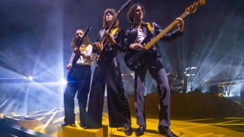 Josh Dewhurst, Tom Ogden and Charlie Salt of Blossoms standing together on stage, all playing guitars, at Eventim Apollo in London on 2 November 2024